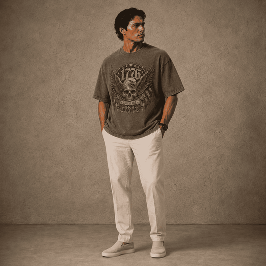 Man wearing a USA 250th Anniversary Shirt 1776 Skull Eagle graphic t-shirt and light-colored pants against a textured wall.