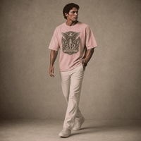 Man wearing a USA 250th Anniversary Shirt pink t-shirt with a graphic design and beige pants against a brown background