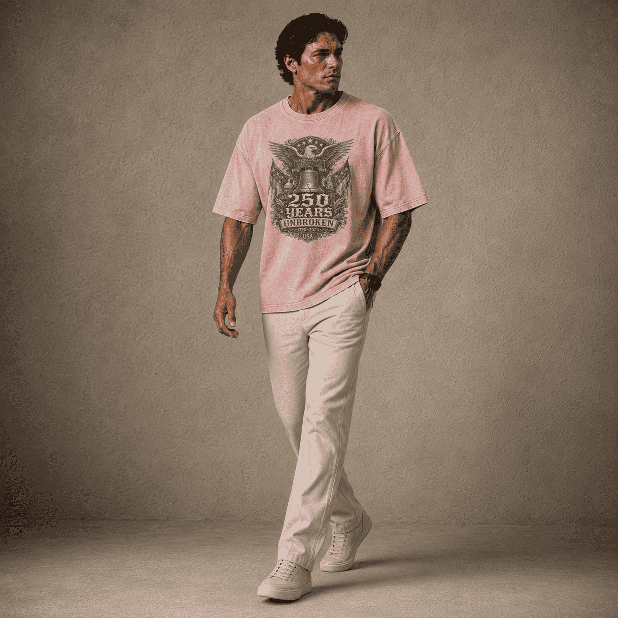 Man wearing a USA 250th Anniversary Shirt pink t-shirt with a graphic design and beige pants against a brown background