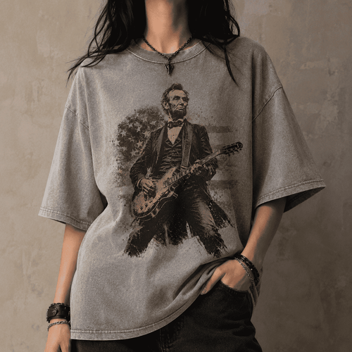 Person wearing a gray t-shirt with a graphic of Abraham Lincoln playing a guitar against a textured wall.