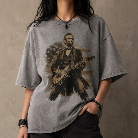 Person wearing a gray t-shirt with a graphic of Abraham Lincoln playing a guitar against a textured wall.