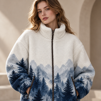 A woman wearing a sherpa fleece zip-up jacket with a blue and white mountain and pine tree landscape print, photographed in a softly lit architectural setting.