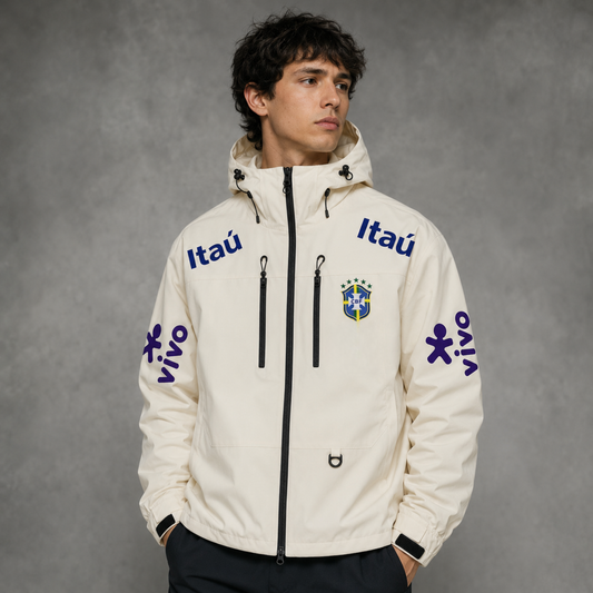 A man wearing a cream-colored Itañ jacket with blue logos and graphics, standing against a textured gray studio background.