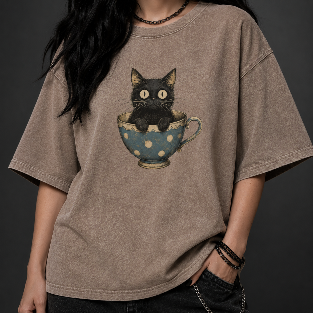 Person wearing a brown t-shirt with a graphic of a black cat in a polka dot teacup.