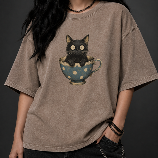 Person wearing a brown t-shirt with a graphic of a black cat in a polka dot teacup.