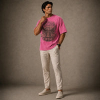 Man wearing a pink t-shirt with text and light-colored pants against a gray background