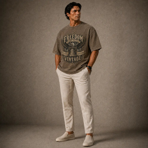 Man wearing a gray t-shirt with 'Freedom Vintage' text and white pants against a brown background