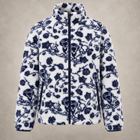 A white sherpa fleece jacket with a navy blue floral and vine pattern, featuring a full-zip front and a high stand-up collar, shown against a textured beige background.