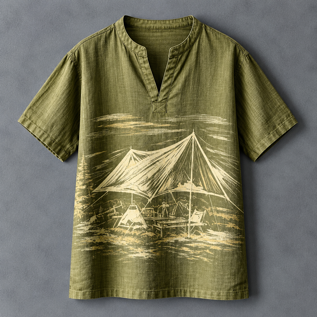 An olive green short-sleeve tunic shirt with a split neckline, featuring a cream-colored graphic print of a beach campsite with a tent and lounge chairs, laid flat against a textured gray background.