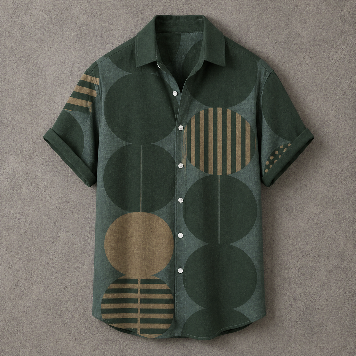 A short-sleeve button-up shirt in dark green with a geometric pattern of large circles and striped oval shapes in tan and olive, laid flat on a textured gray background.