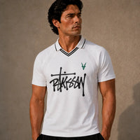 Man wearing a white polo shirt with black text and green logo against a beige background