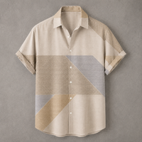A short-sleeve button-up shirt with a geometric color-block pattern in beige, tan, and light gray, displayed flat against a textured gray background.