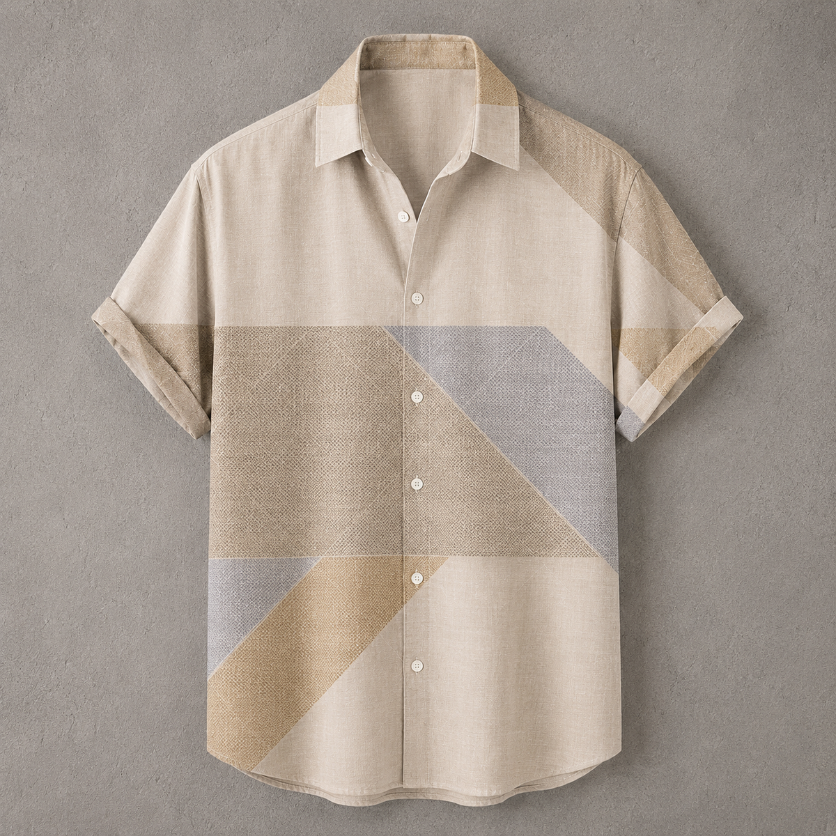 A short-sleeve button-up shirt with a geometric color-block pattern in beige, tan, and light gray, displayed flat against a textured gray background.