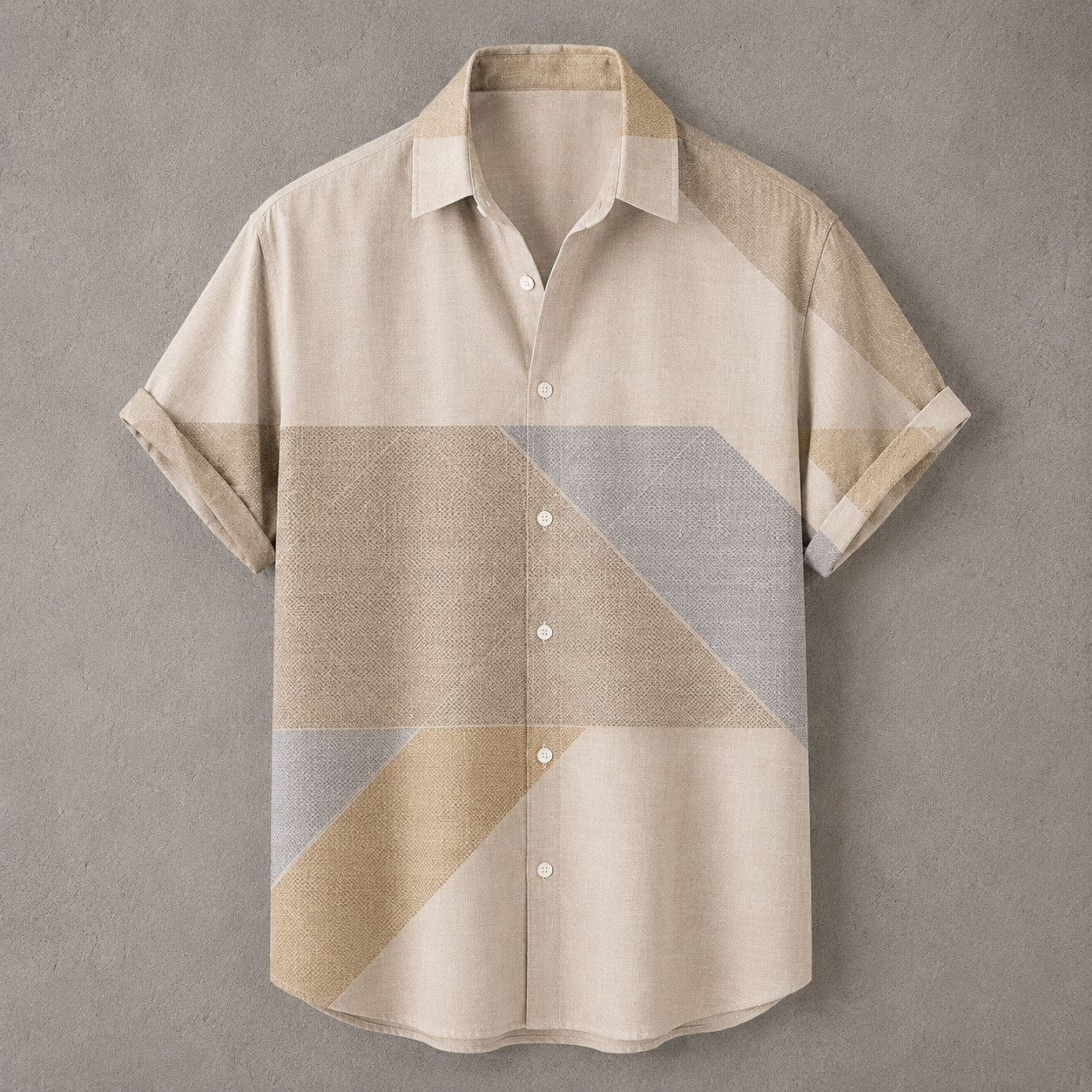 A short-sleeve button-up shirt with a geometric color-block pattern in beige, tan, and light gray, displayed flat against a textured gray background.