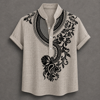 A men's short-sleeve button-up shirt in a light beige linen-like fabric, featuring a black ornate floral and scroll pattern printed on the chest and shoulders, set against a dark gray background.