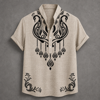 A beige short-sleeve button-up shirt with black ornate tribal-style embroidery on the chest and lower hem, displayed flat against a textured gray background.