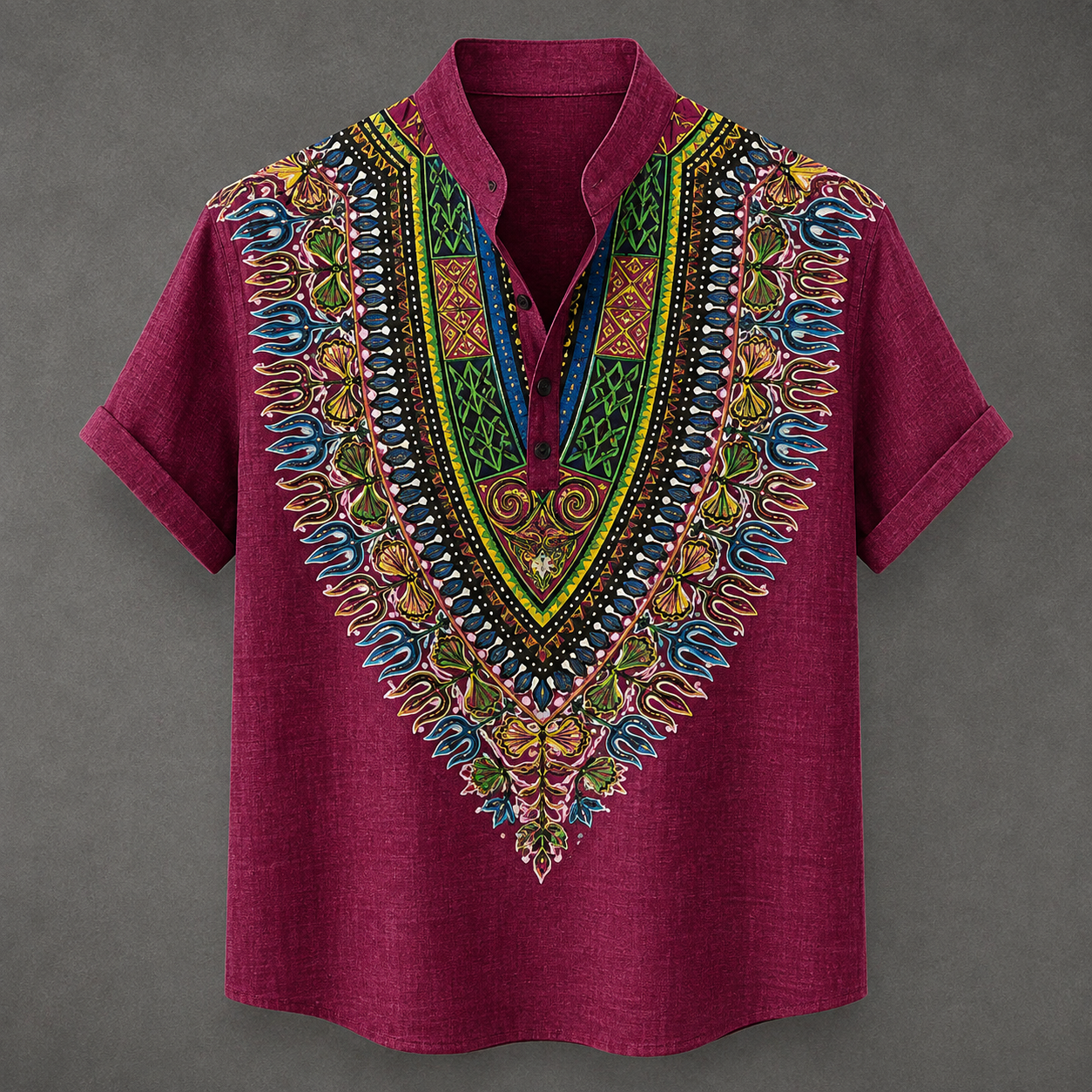 A short-sleeve button-up shirt in deep magenta, featuring a large, vibrant, multicolored African dashiki-style print on the V-neck panel, collar, and sleeve cuffs, set against a dark gray background.