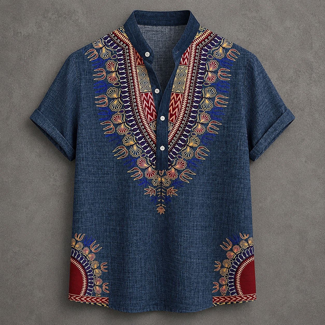 A short-sleeve button-up shirt in blue denim-like fabric with colorful African dashiki-style embroidery around the V-neck and lower hem, shown flat against a textured gray background.