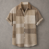 A short-sleeve button-up shirt with a textured, speckled patchwork pattern in shades of beige, tan, and brown, laid flat against a textured gray background.