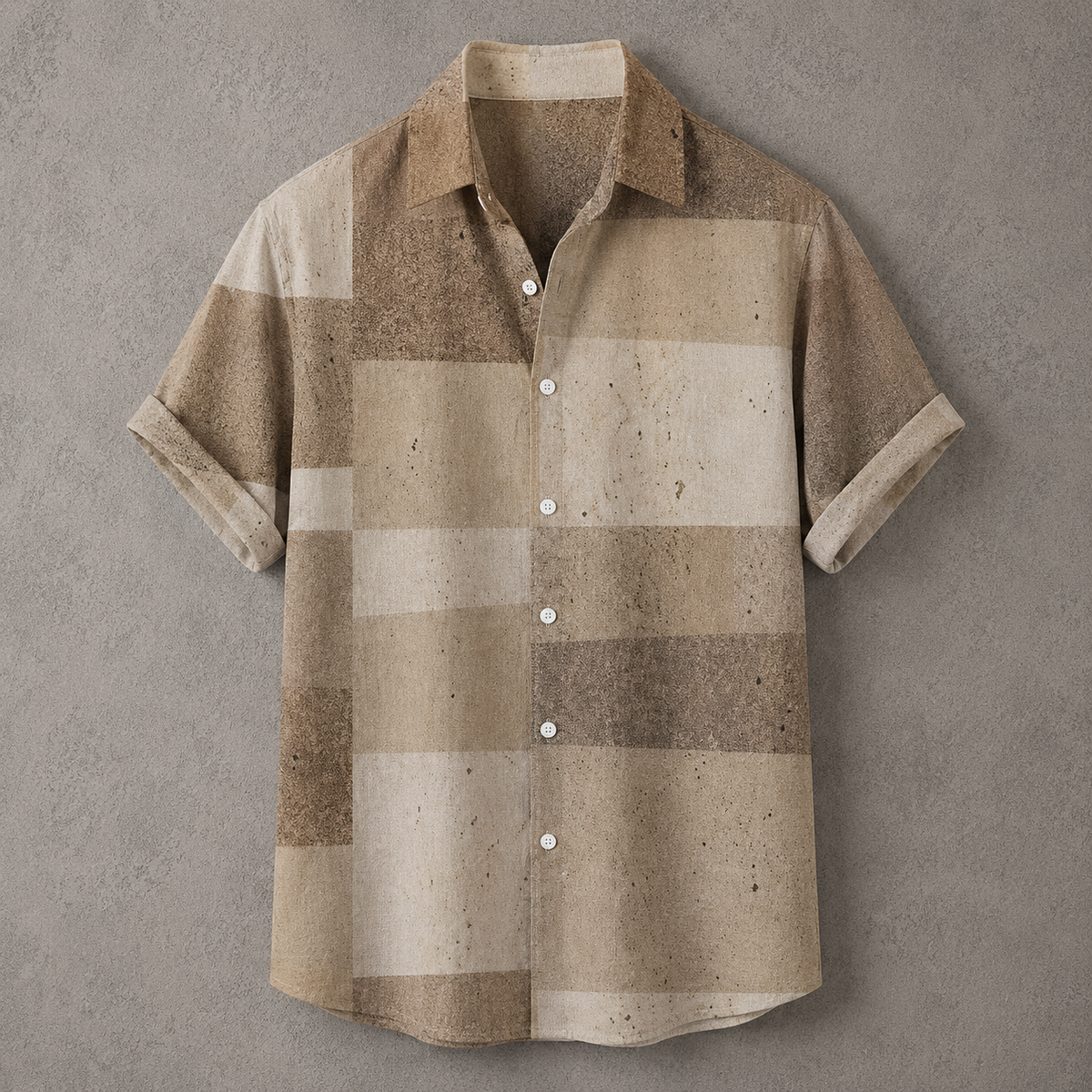 A short-sleeve button-up shirt with a textured, speckled patchwork pattern in shades of beige, tan, and brown, laid flat against a textured gray background.