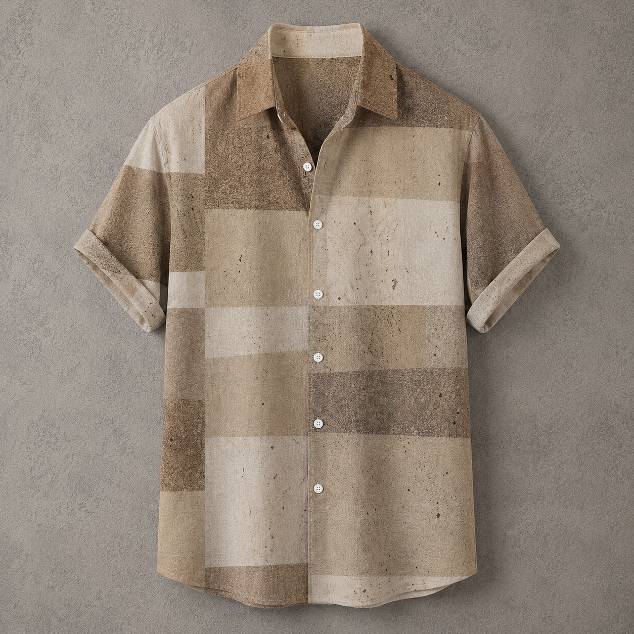 A short-sleeve button-up shirt with a textured, speckled patchwork pattern in shades of beige, tan, and brown, laid flat against a textured gray background.
