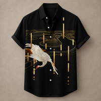 A black short-sleeve button-up shirt with a printed design featuring a white crane and gold abstract water and vertical line patterns, displayed against a neutral beige background.