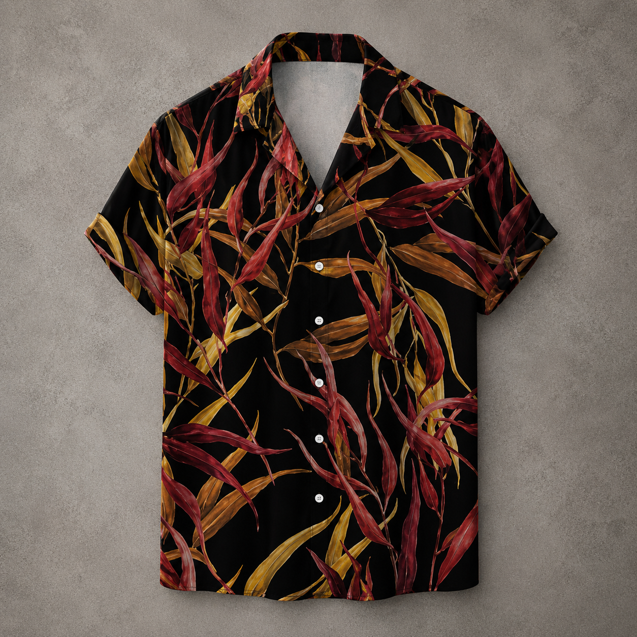 A short-sleeve button-up camp shirt with a black background and an all-over tropical leaf print in red, burgundy, and yellow, displayed flat against a textured gray background.