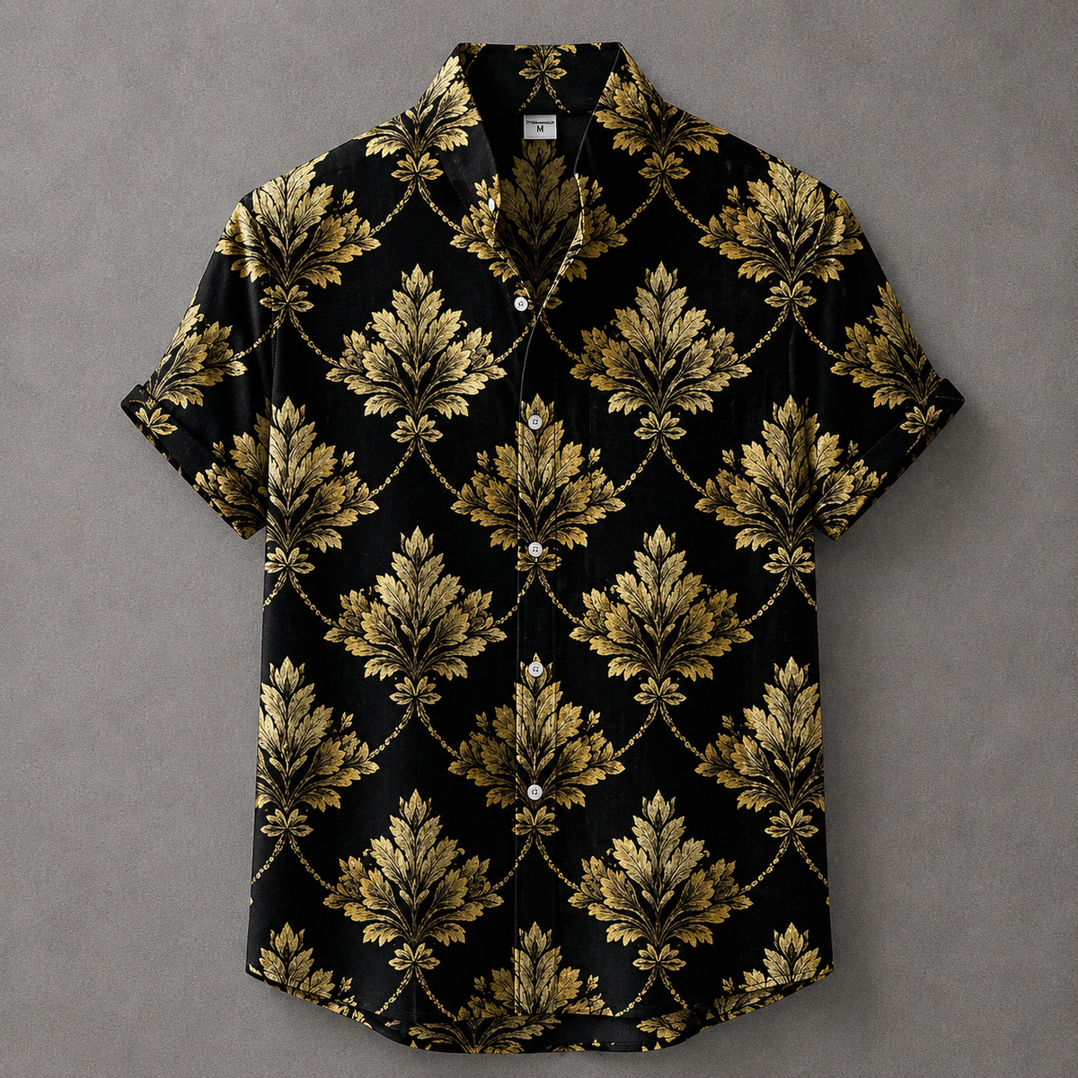A short-sleeve button-up camp shirt with a black background and an ornate gold damask pattern, laid flat on a textured gray background.
