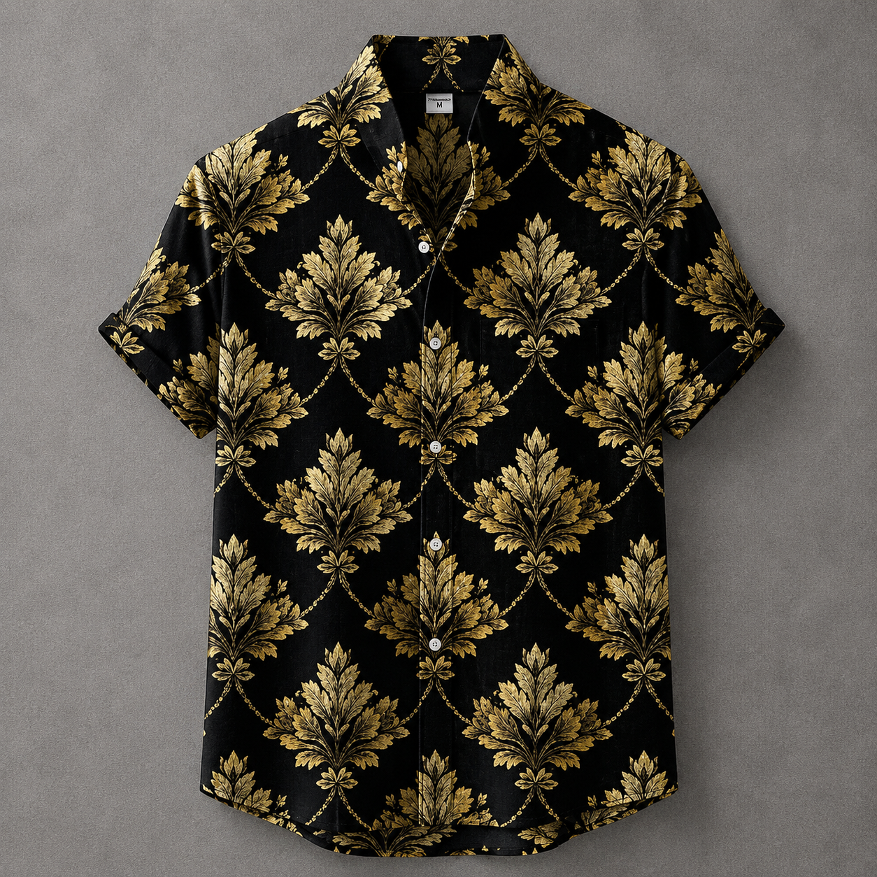 A short-sleeve button-up camp shirt with a black background and an ornate gold damask pattern, laid flat on a textured gray background.