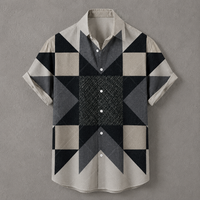 A short-sleeve button-up shirt with a geometric patchwork pattern in beige, gray, and black, displayed flat against a textured gray background.