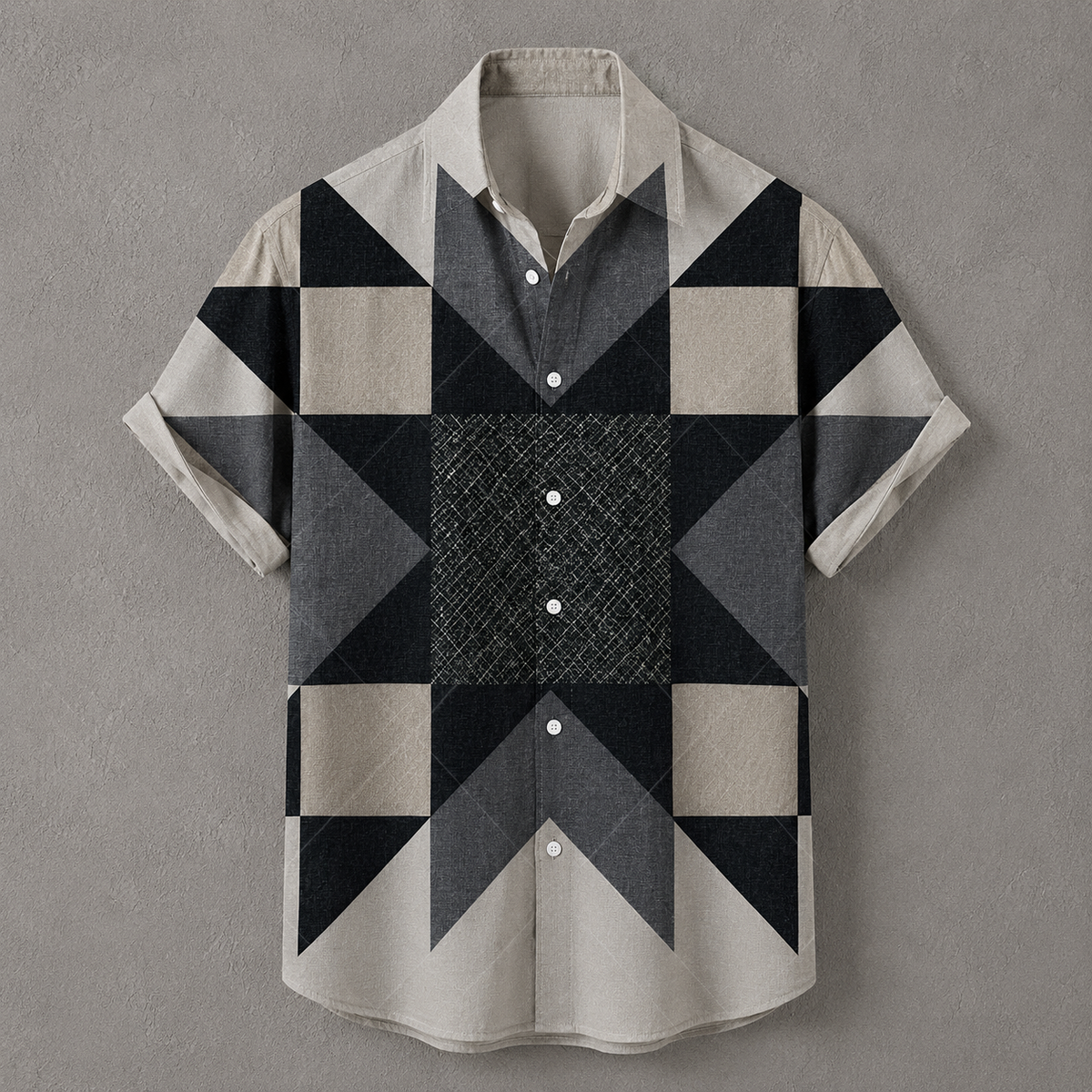 A short-sleeve button-up shirt with a geometric patchwork pattern in beige, gray, and black, displayed flat against a textured gray background.