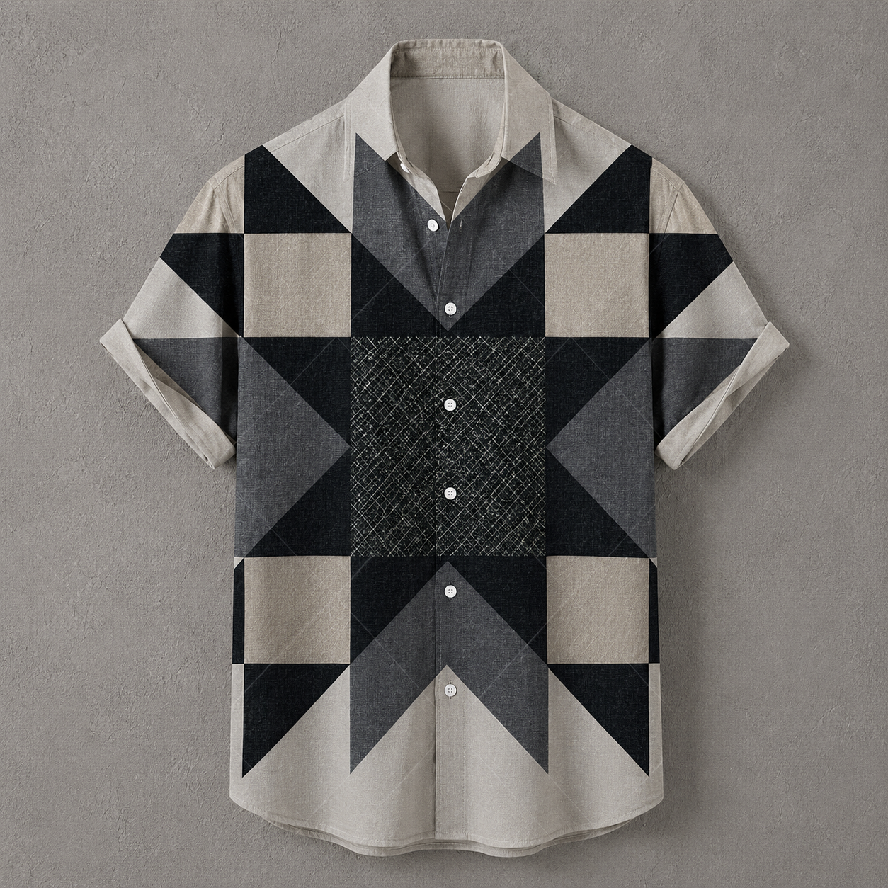 A short-sleeve button-up shirt with a geometric patchwork pattern in beige, gray, and black, displayed flat against a textured gray background.