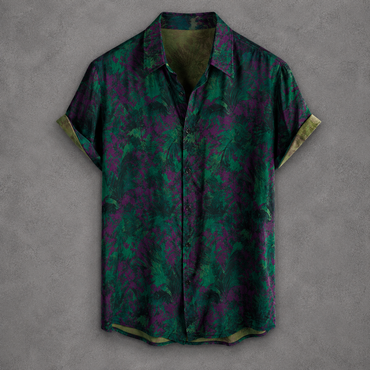 A short-sleeve button-up shirt with a green and purple abstract floral pattern, displayed flat against a textured gray background.