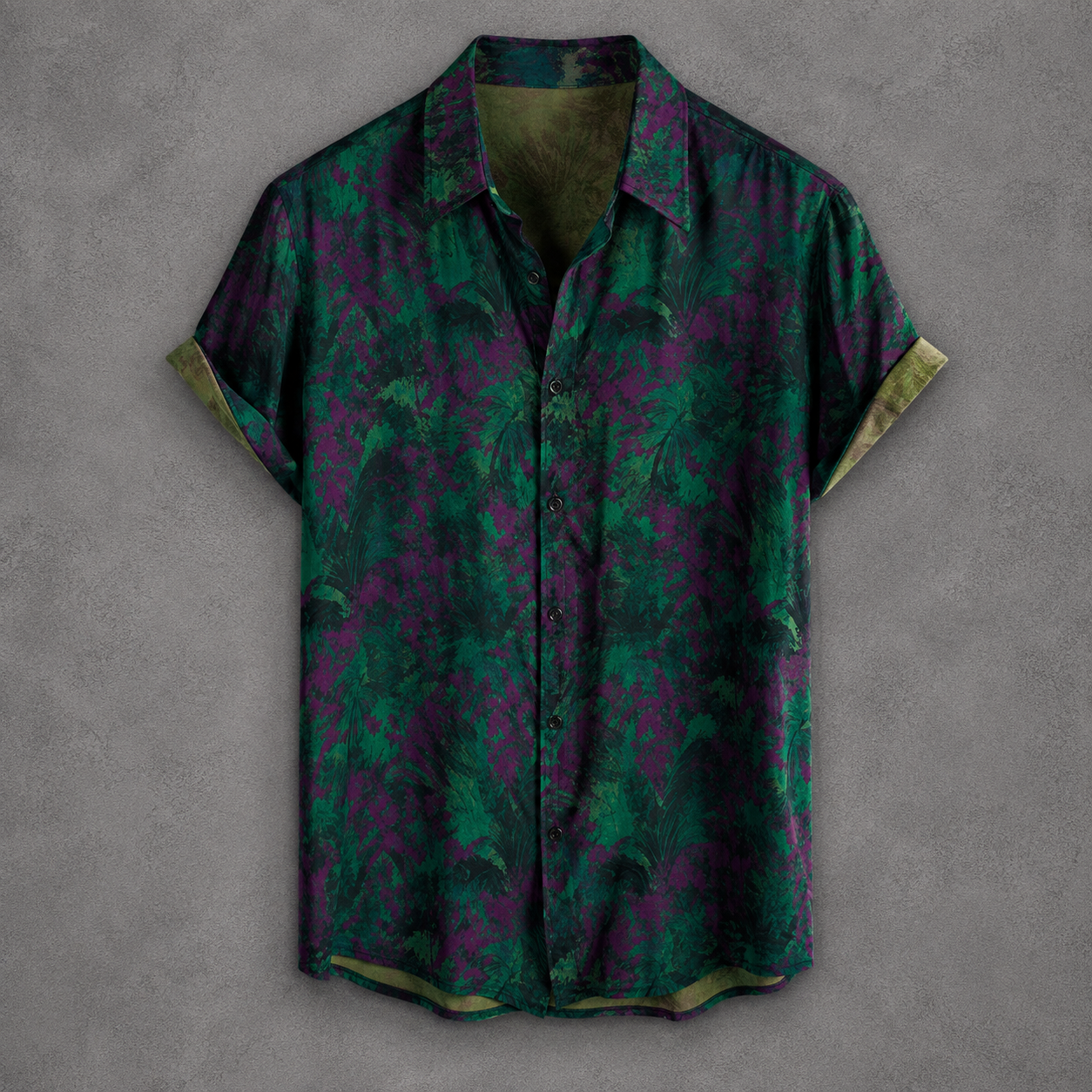 A short-sleeve button-up shirt with a green and purple abstract floral pattern, displayed flat against a textured gray background.
