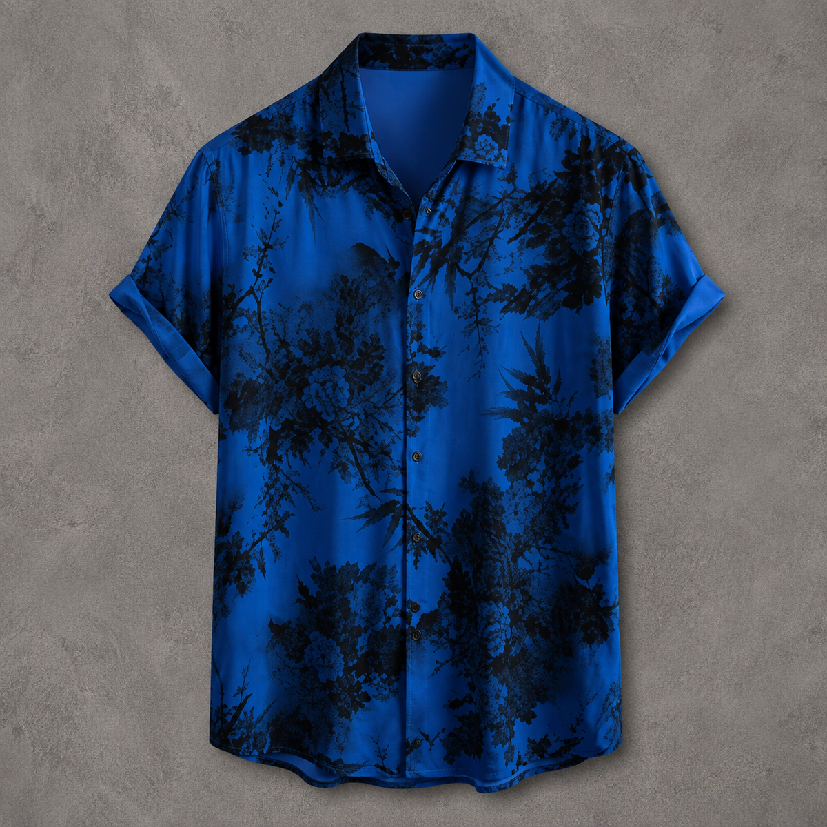 A short-sleeve button-up shirt in vibrant royal blue with a black tropical floral and branch print, displayed flat against a textured gray background.
