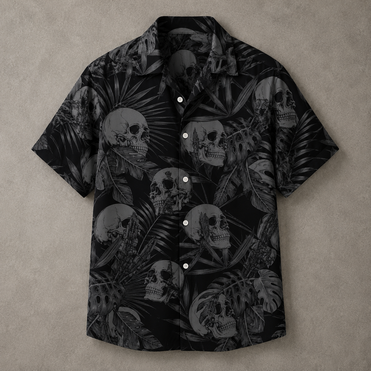 A short-sleeve button-up camp shirt with a black and gray tropical print featuring skulls and palm leaves, laid flat on a textured gray background.