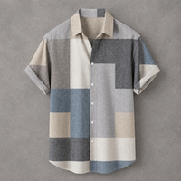 A short-sleeve button-up shirt with a geometric patchwork pattern in beige, gray, blue, and white, displayed flat against a textured gray background.