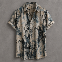 A short-sleeve button-up shirt with a distressed, abstract tie-dye or marble-like print in beige, slate blue, and charcoal gray, laid flat against a textured gray background.