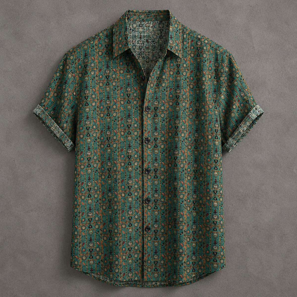 A short-sleeve button-up shirt with a dense, small-scale geometric and floral pattern in teal green, brown, and black, laid flat against a textured gray background.