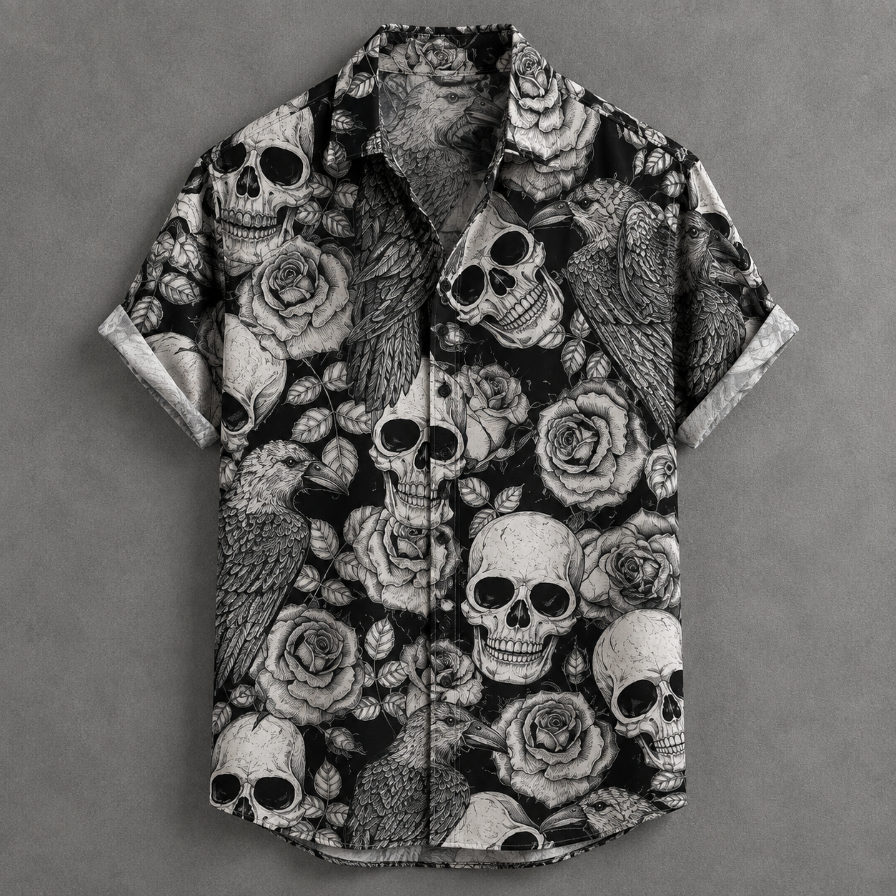 A short-sleeve button-up shirt with a black and white graphic print featuring skulls, roses, and birds, laid flat on a textured gray background.