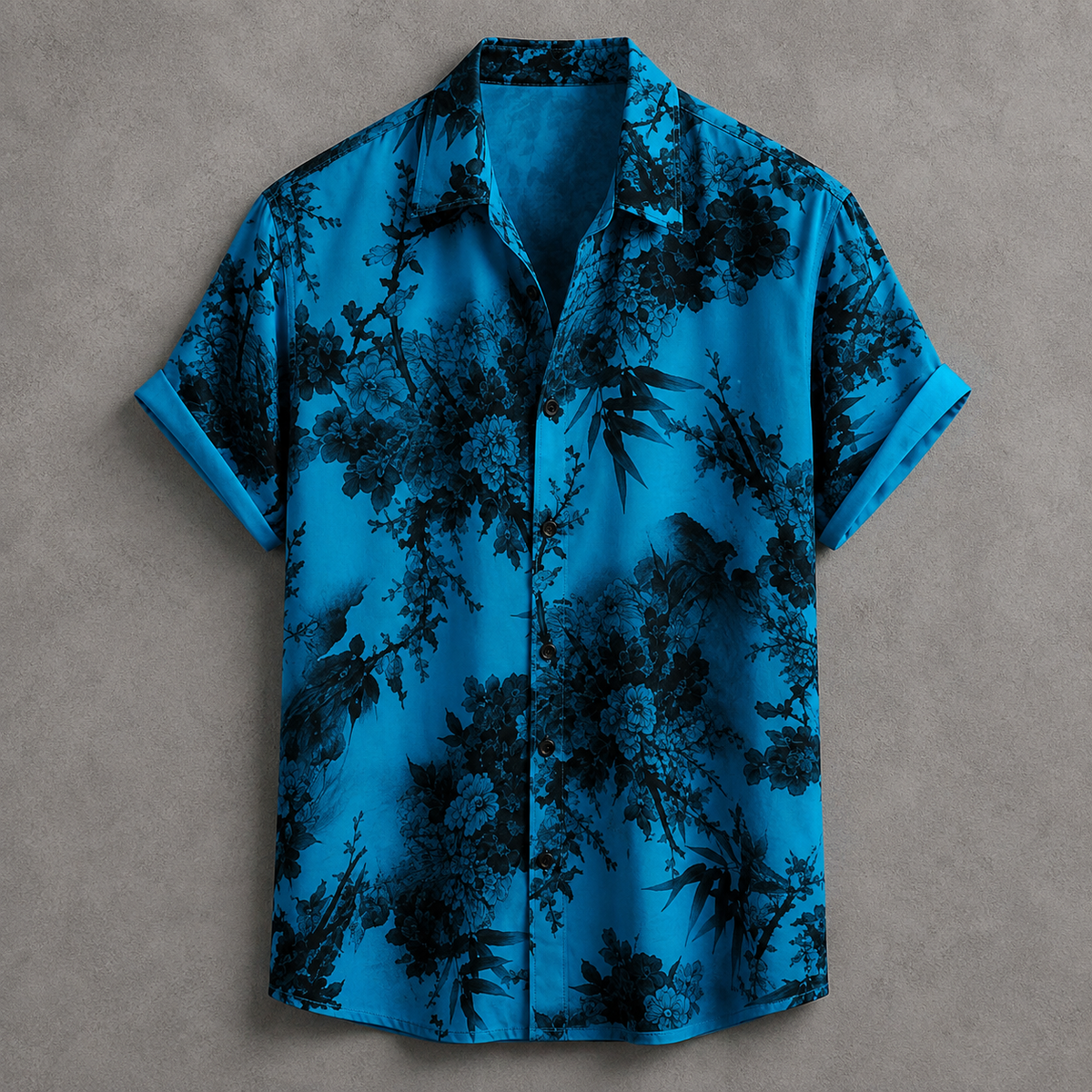 A short-sleeve button-up shirt with a vibrant blue base and a black bamboo and foliage print, displayed flat against a textured gray background.