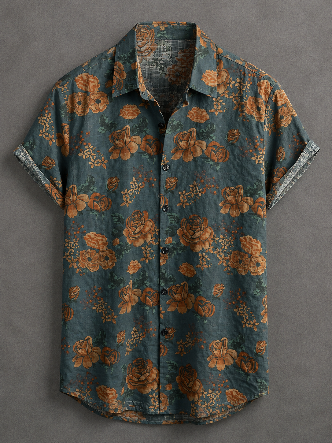 A short-sleeve button-up shirt with an all-over floral print in rust orange and green on a dark teal-blue background, displayed flat against a textured gray backdrop.