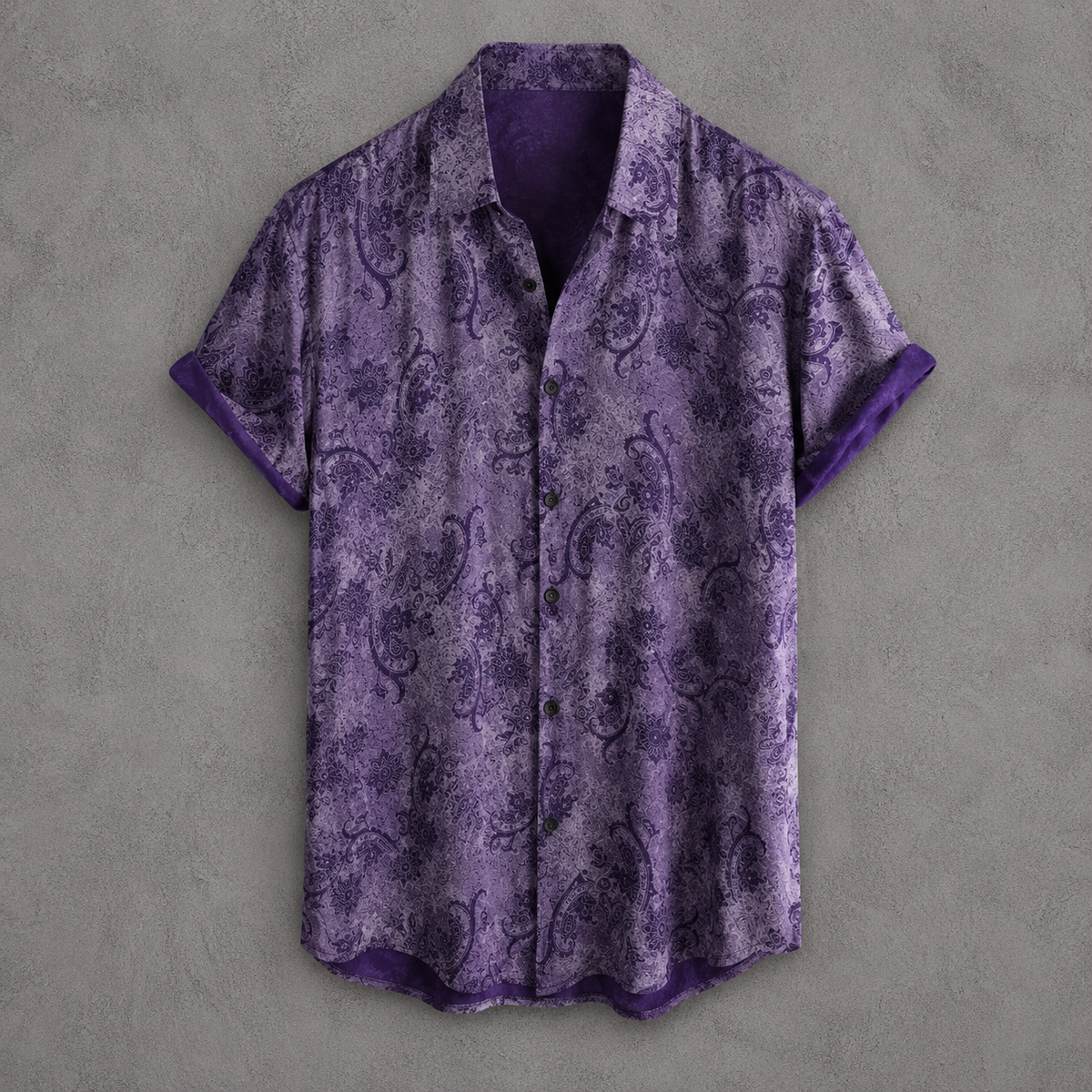 A short-sleeve button-up shirt in purple with a dark paisley pattern and solid purple trim, displayed flat against a textured gray background.