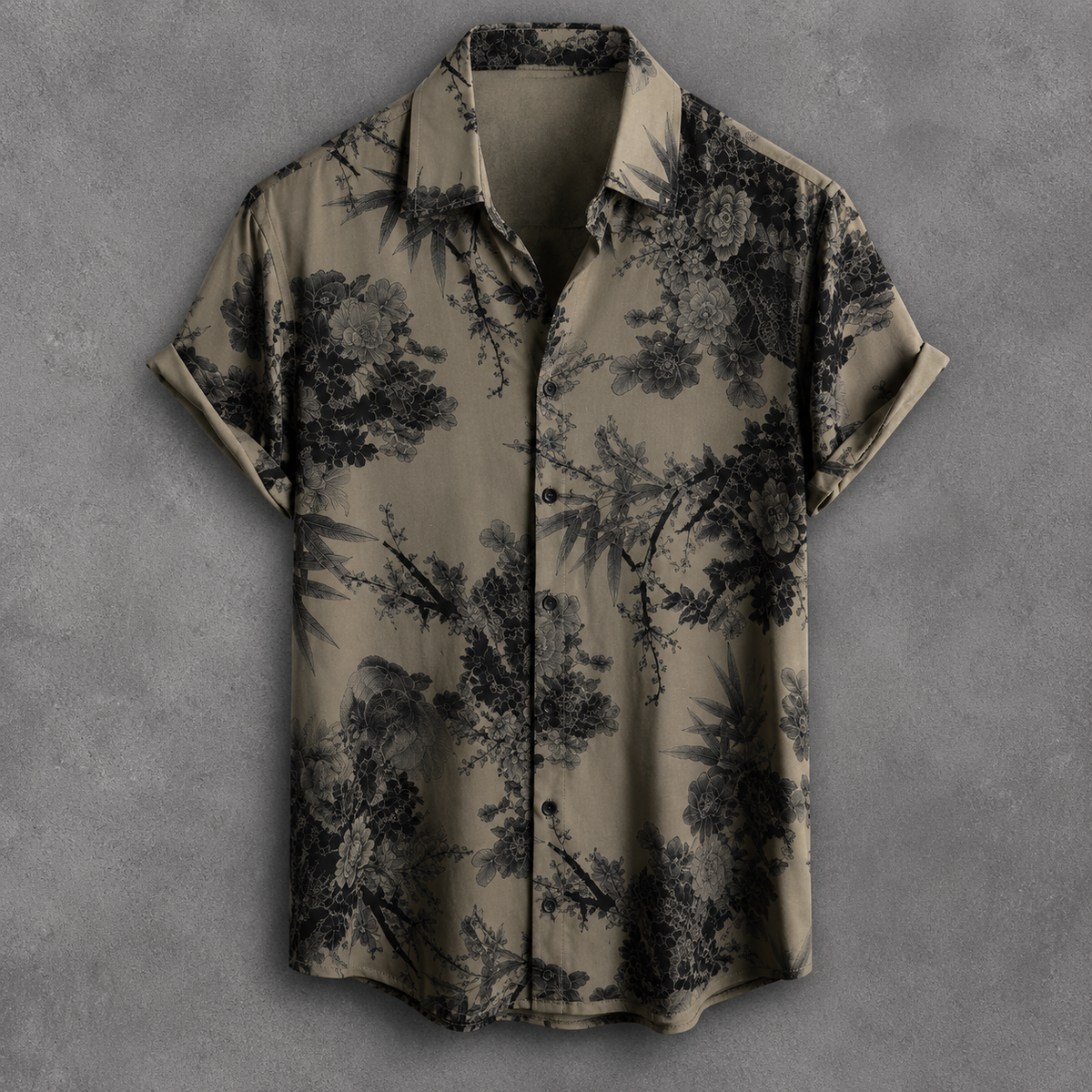 A short-sleeve button-up shirt with a black tropical floral and bamboo print on a muted olive-beige background, displayed flat against a textured gray backdrop.
