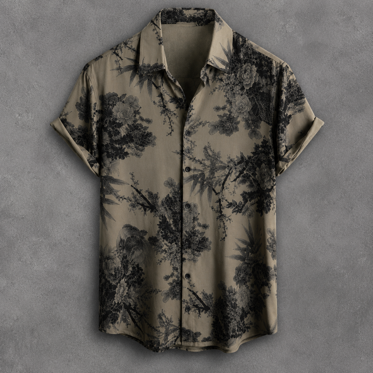 A short-sleeve button-up shirt with a black tropical floral and bamboo print on a muted olive-beige background, displayed flat against a textured gray backdrop.