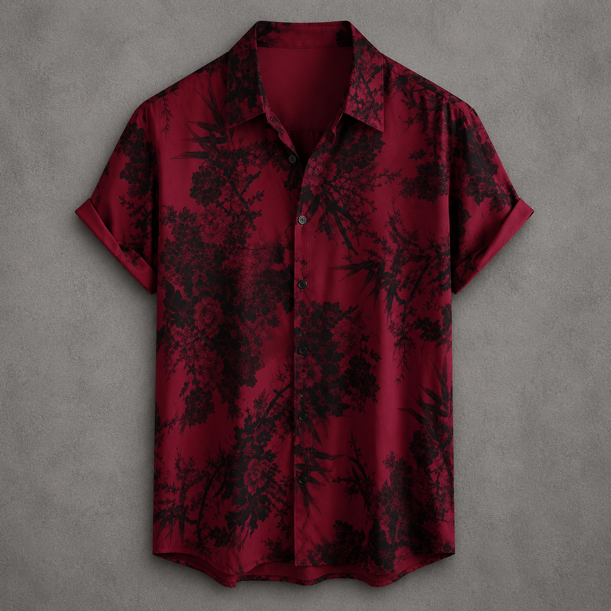 A short-sleeve button-up shirt in deep red with a black floral and bamboo print, displayed flat against a textured gray background.