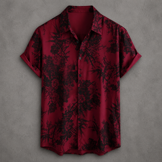 A short-sleeve button-up shirt in deep red with a black floral and bamboo print, displayed flat against a textured gray background.
