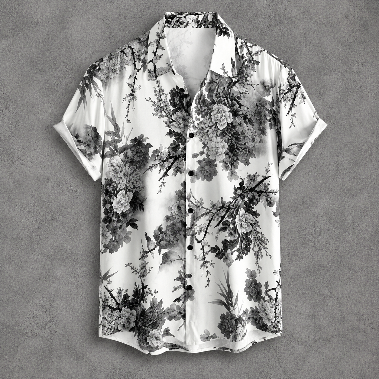 A short-sleeve button-up shirt with a black and white floral and branch print, displayed flat against a textured gray background.