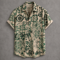 A short-sleeve button-up shirt with a beige base and an intricate green floral and paisley pattern, laid flat against a textured gray background.