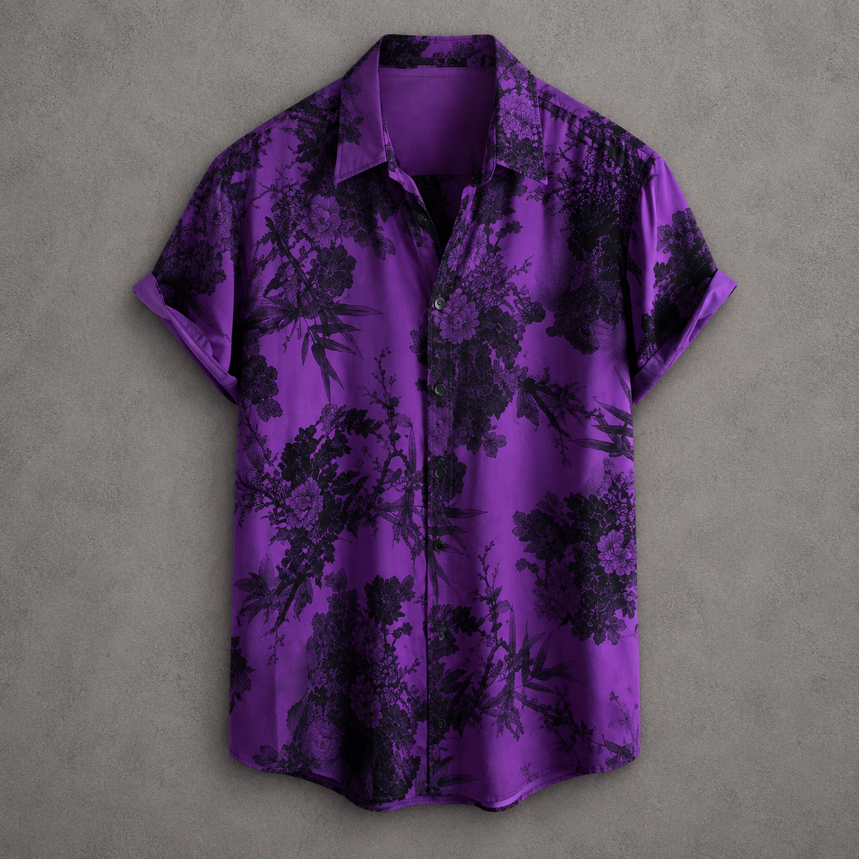 A short-sleeve button-up shirt in vibrant purple with a black botanical and floral print, displayed flat against a textured gray background.